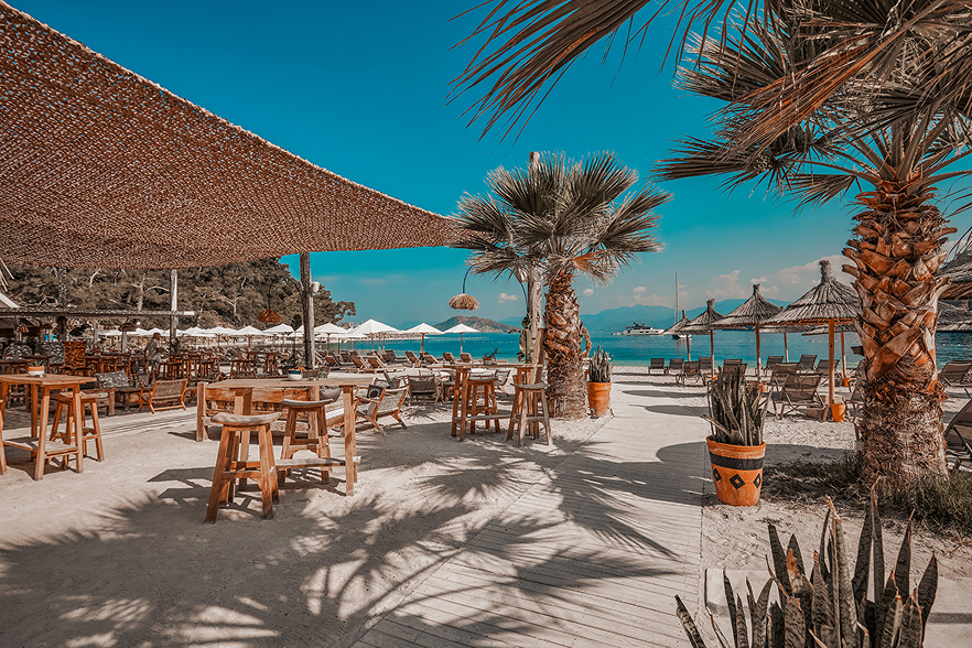 Sea Me Beach Fethiye plaj restoranında gölgelik altında ahşap masa ve sandalyeler